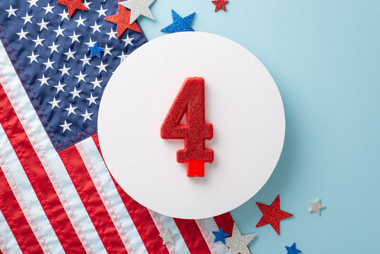 Top view of festive party decorations: patriotic shimmering stars, number 4 candle on round card, and American flag on a pastel blue backdrop - Powered by Adobe
