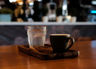 Hot coffee in a brown ceramic mug served with cold drinking water on the table in the coffee shop.