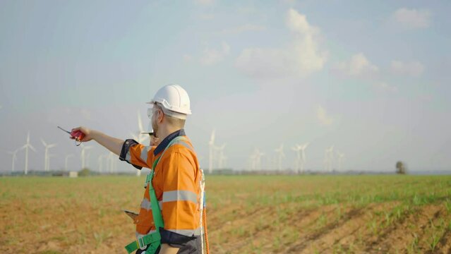Caucasian engineer man in hard hat walking and discuss together with co-worker man hold tablet stay in front of row of windmill or wind turbine, wind turbine generate electricity, Environmentally frie