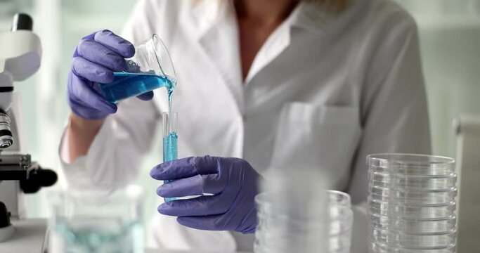 Laboratory assistant pours blue chemical into test tube. Scientific research in chemical industry