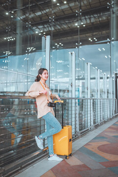Happy attractive asian woman passenger traveler with a yellow suitcase at the modern airport terminal, copy space, Tourist journey trip concept