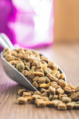 Dry kibble pet food. Dog or cat food in scoop on wooden table.
