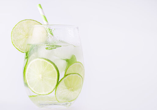 Summer lemonade with basil and lime on white background. One fresh summer cocktail with basil, green lemon and ice cubes. Drink concept