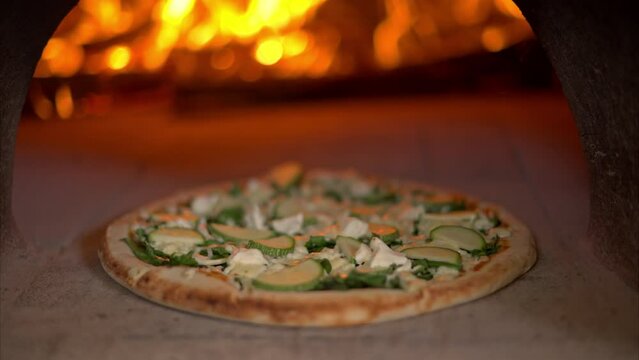 Slow motion close up of a squash and goat cheese pizza cooked baked inside a traditional stone oven with wood burning and fire flames