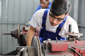 Multiethnic technicain mechanic or worker man in protective uniform using metal lathe machine operate polishing car disc brake at garage. Maintenance automotive and inspecting vehicle part concept
