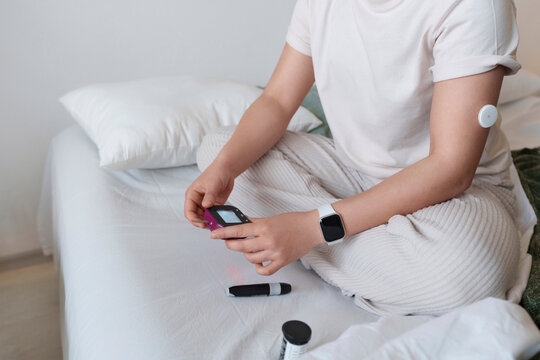 Woman holding glucometer sitting on bed at home