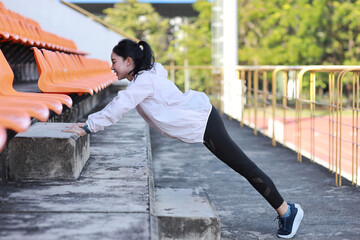 Strong and beautiful asian fitness female sportswoman doing pushups excercise and workout at stadium while akimbo and looking away