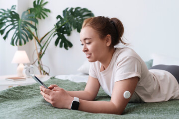 Woman with diabetes using smart phone lying on bed at home
