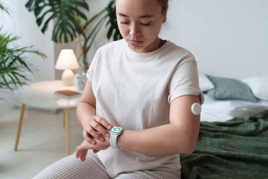 Woman with diabetes checking smart watch sitting on bed at home