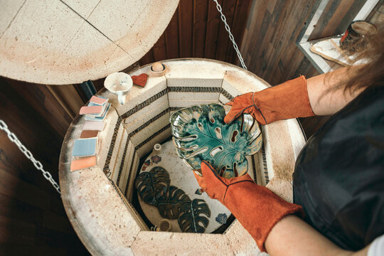 Potter holding ceramic leaf near kiln at workshop