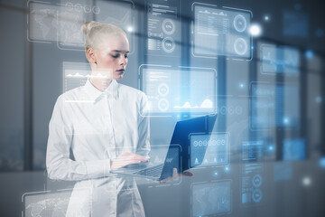 Attractive blonde woman using laptop with glowing business chart holograms on blurry office...