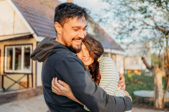 Cheerful couple embracing in front yard with house in background