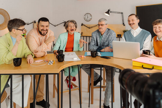 Group ofwomen and men sitting at studio table recording video on the camera