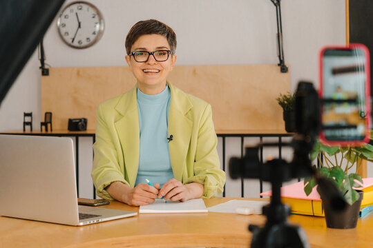 Businesswoman with eyeglasses sitting at table in studio filming online class