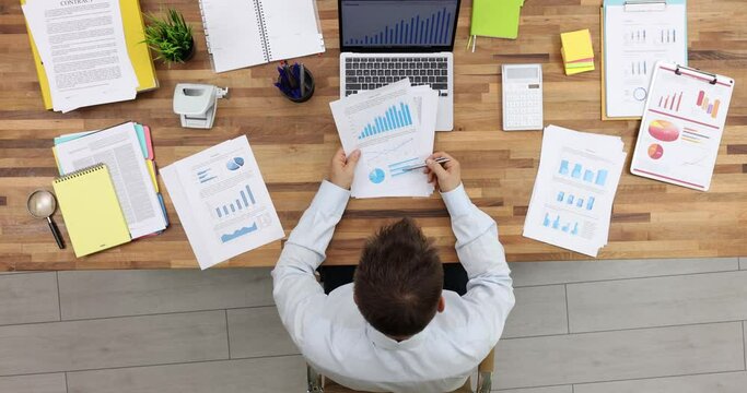Manager working with financial reports sitting at table in office top view. Businessman checking financial report presentation data