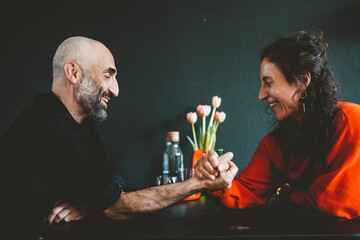 Happy woman arm wrestling with man in front of black wall