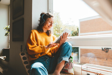 Smiling woman using tablet PC sitting near window at home
