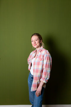 Confident young woman wearing plaid shirt standing in front of green wall