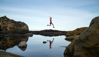 Woman with arms raised jumping over rocks