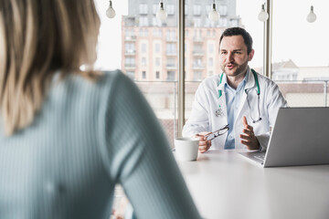 Doctor consulting patient sitting at table in clinic
