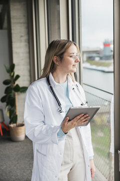 Female doctor looking out of window holding tablet PC at hospital