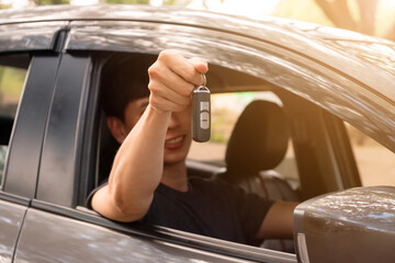 Close-up shot of young Asian man sitting in a car and handing out the car keys.