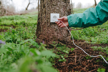 Man connecting electric plug in outlet on tree trunk