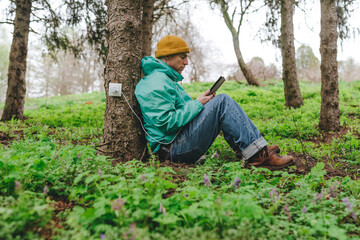 Man using tablet PC connected with outlet on tree trunk