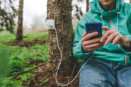 Man using smart phone connected with outlet on tree trunk