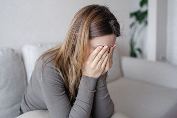 Young depressed woman sitting on sofa in living room. She feeling sad and worried suffering...