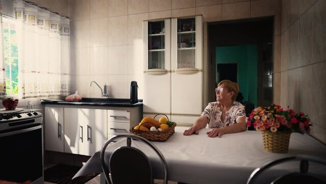 Lonely senior woman sitting alone in kitchen table. Old age lifestyle of elderly person in solitude and isolation