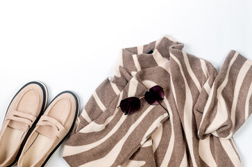 Black pants, beige knitted oversize sweater, beige suede loafer on white background.