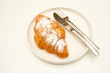 Tasty croissant with sprinkling icing sugar on white plate on white background. 
