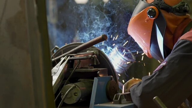 Welding work close-up. Welder worker weld pipe in protective helmet. Sparks fly out. Welding shop at Construction of Oil, Natural Gas and Fuels Transport Pipeline. Industrial Manufacturing Factory