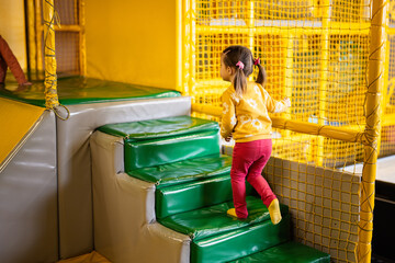 Little girl step up in stairs at yellow playground park. Child in active entertaiments.