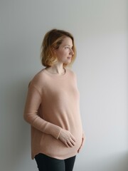 Pregnant woman in a pink sweater on a gray background.