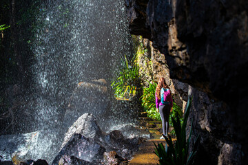 A beautiful girl enjoys a walk behind a spectacular tall waterfall while hiking the Warrie Circuit trail in Springbrook National Park, Gold Coast, Queensland, Australia