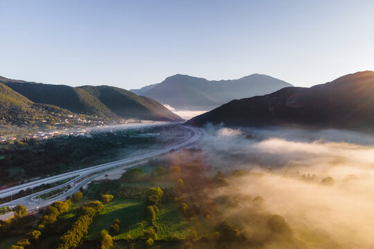Aerial view of vehicles on the highway road at sunrise with low clouds and fog among the mountains in Psaka, Epirus, Greece.