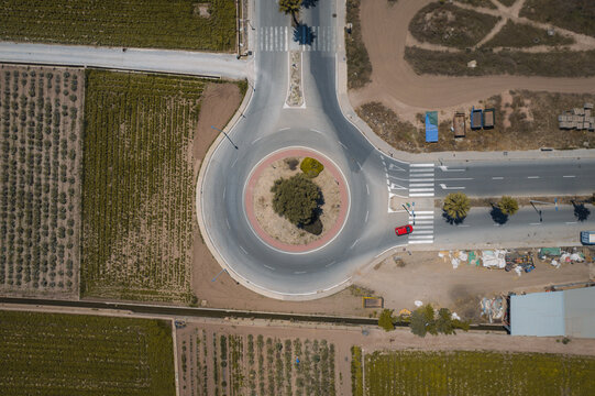 Aerial view of a roundabout with a red car driving on the side in agricultural fields, Alboraia, Valencia, Spain.