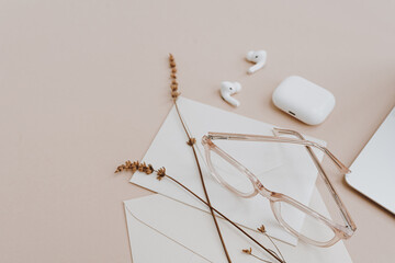 Aesthetic styled women home office workspace desk. Glasses, earphones, envelopes, dried grass on tan beige table. Elegant modern work at home concept