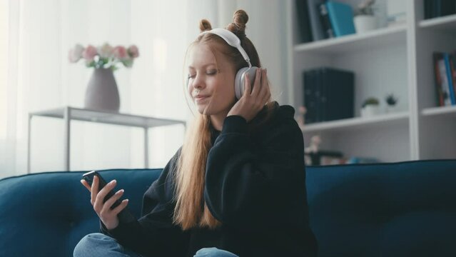 Happy teenage girl in headphones listening to music and using her smartphone