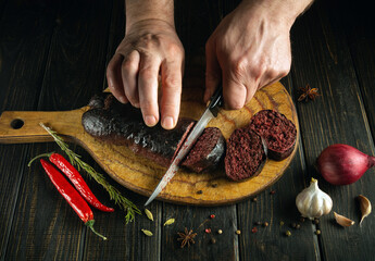 The cook cuts blood sausage with a knife on a cutting kitchen board. Cooking a national dish on the...