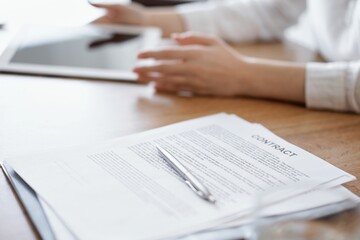 Contract papers are lying at the wooden desk while business people discussing something at the wooden desk at the background. Teamwork, partnership, contract signing concept.