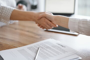 Business people shaking hands above contract papers just signed on the wooden table, close up. Lawyers at work. Partnership, success concept.
