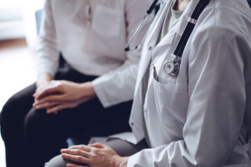 Doctor and patient sitting at sofa. The focus is on female physician's hands reassuring woman, close up. Medicine concept.