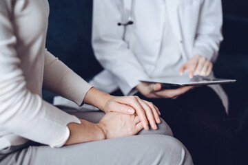 Fototapeta premium Doctor and patient sitting at sofa in clinic office. The focus is on female woman's hands, close up. Medicine concept.