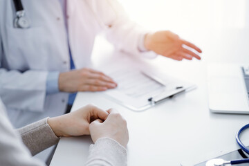 Doctor and patient discussing current health questions while sitting at the table in clinic office, only hands closeup. Medicine concept.