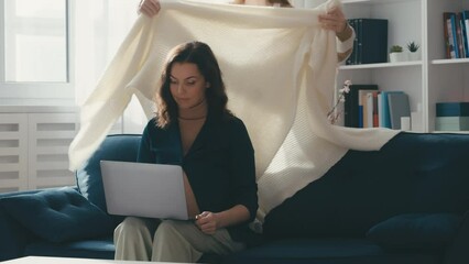Caring teen girl bringing a blanket to pregnant mother working on laptop, love - Powered by Adobe