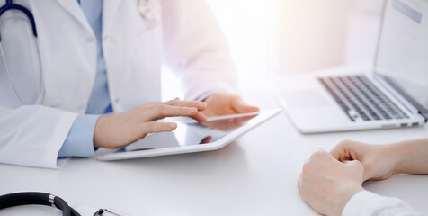 Stethoscope lying on the tablet computer in front of a doctor and patient sitting opposite each other and using tablet computer at the background . Medicine, healthcare concept.
