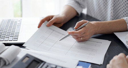 Female accountant pointing with a pen into audit paper while explaining tax counting results, close up. Business audit and finance concepts.